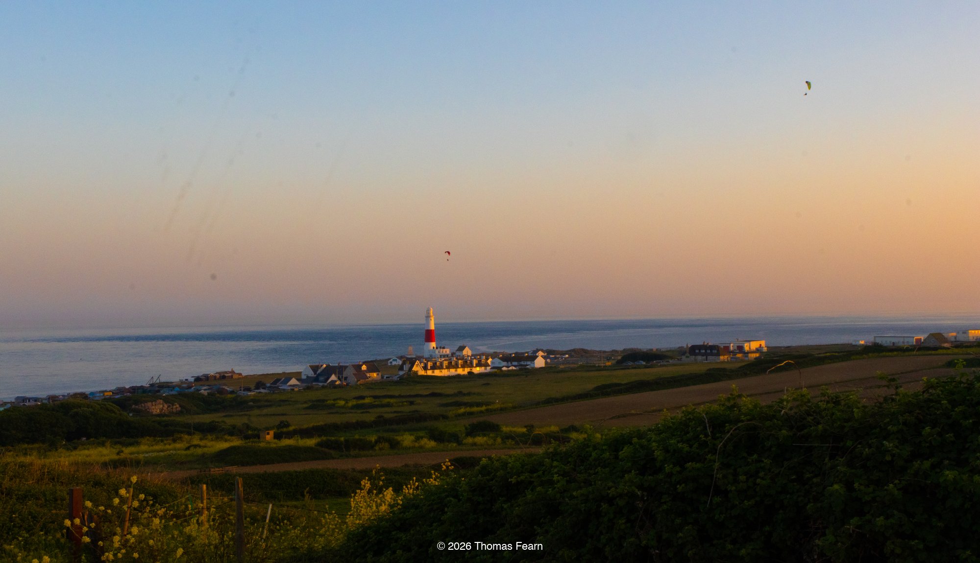 Lighthouse and paragliders on the coast at sunset